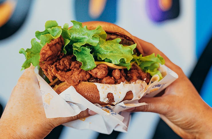 two hands holding a fried chicken sandwich dripping with sauce