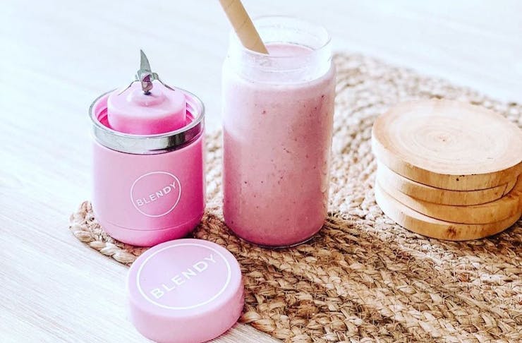 A pink blender sits beside a delicious pink smoothie. 