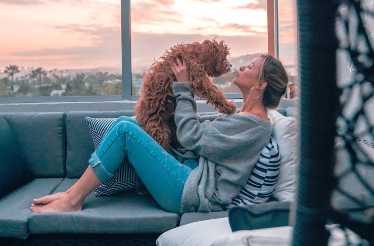 A woman sits on a rooftop couch cuddling a small fluffy dog.