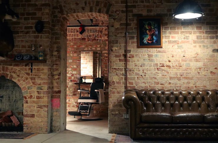 Interior of Ugly Mens Barber In Perth, exposed bricks, leather couches and a barber chair are inside.