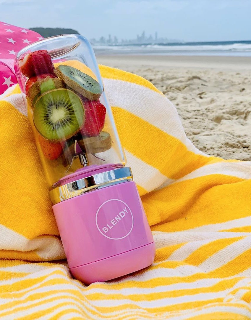 A portable blender sits on a yellow towel on the beach. 