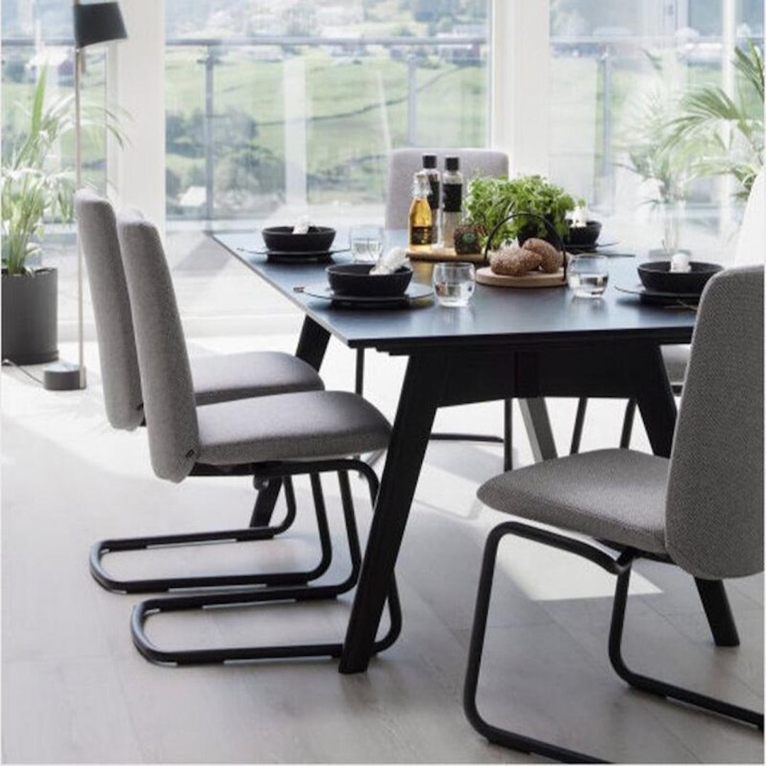 Plush chairs surround a black wooden table with thin legs. 