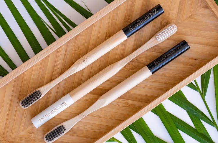 A picture of wooden toothbrushes sitting on a wooden board with a palm frond underneath.