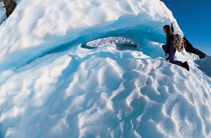 A woman peers into a blue crevasse in the mountains at Fox Glacier, one of the best things to do on the west coast.