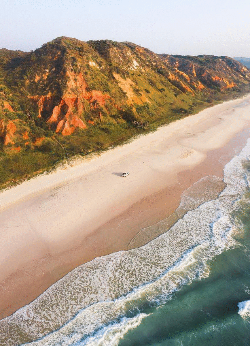A secluded beach stretches along a red sand soaring mountain and ocean.