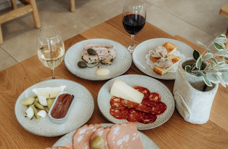 a table full of various plates with salumi and aperitivo dishes with a glass of wine