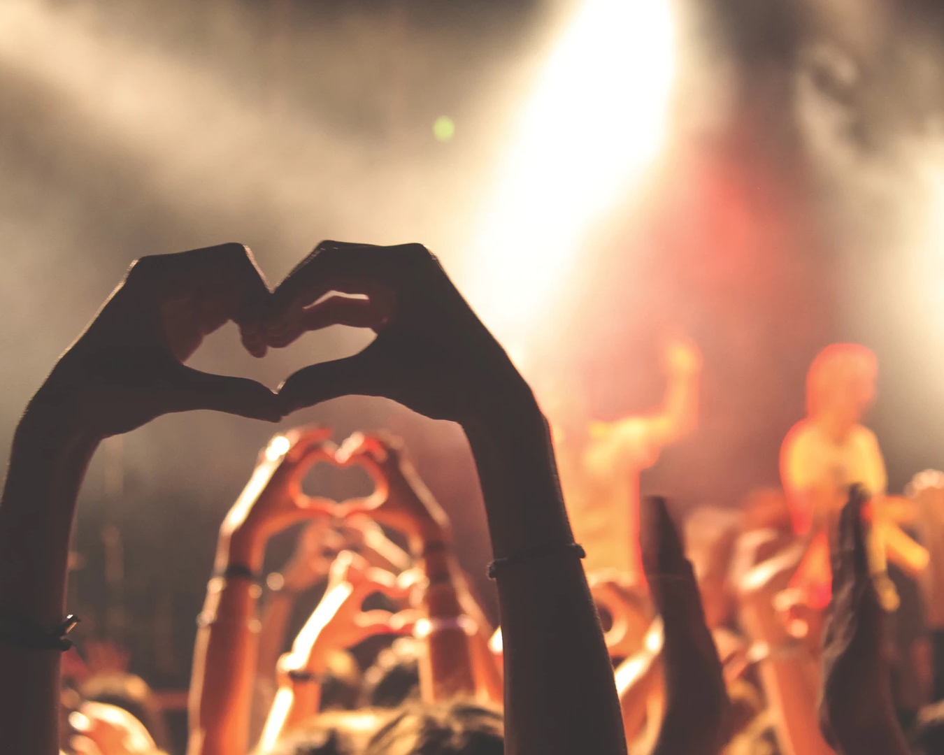 The backs of people at a concert making heart shapes with their hands. 