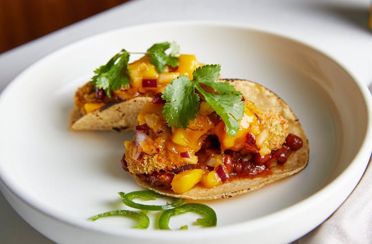 Two crispy avo tacos sit on a plate topped with mango salsa.
