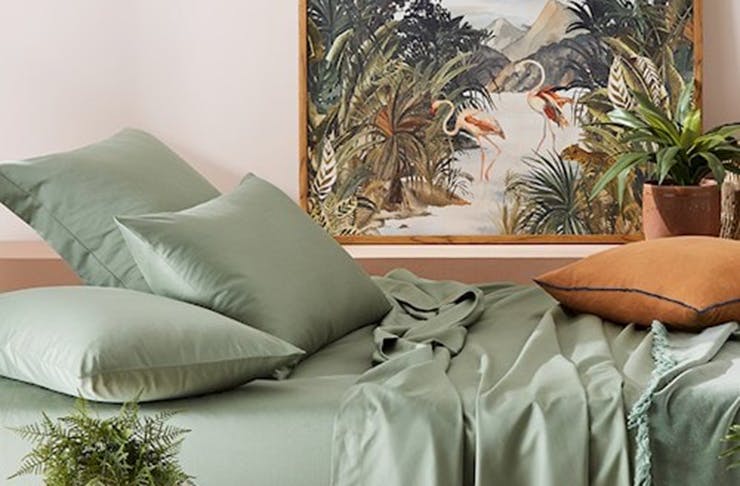 A bed with a light green sheet set and a painting on the wall.