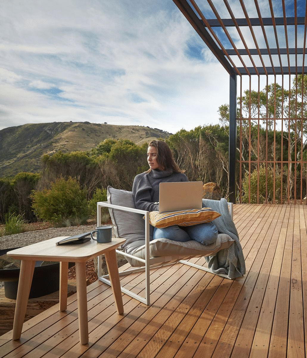 A woman sits in a chair with a laptop in her lap, overlooking the Bass Strait.