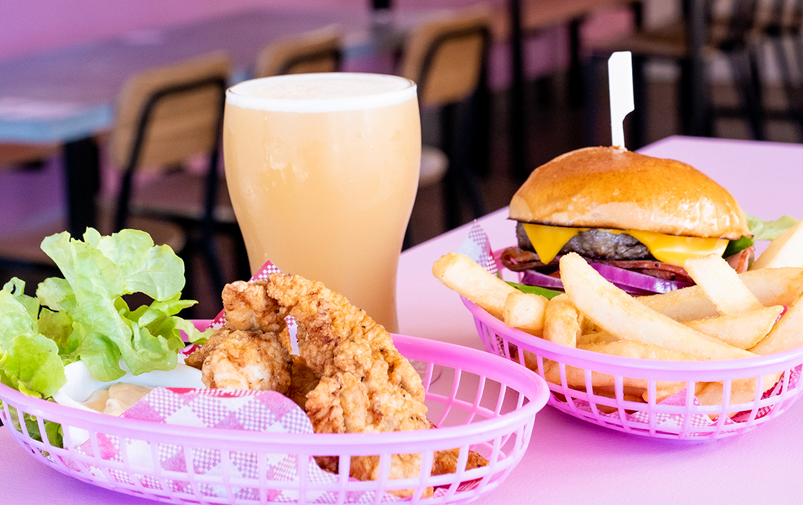 Delicious burger, fries, crispy chicken and drink sitting on a pink table top