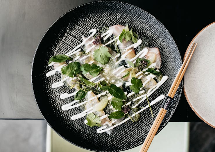 An aerial shot of a plate of Kingfish sashimi drizzled in a white sauce.