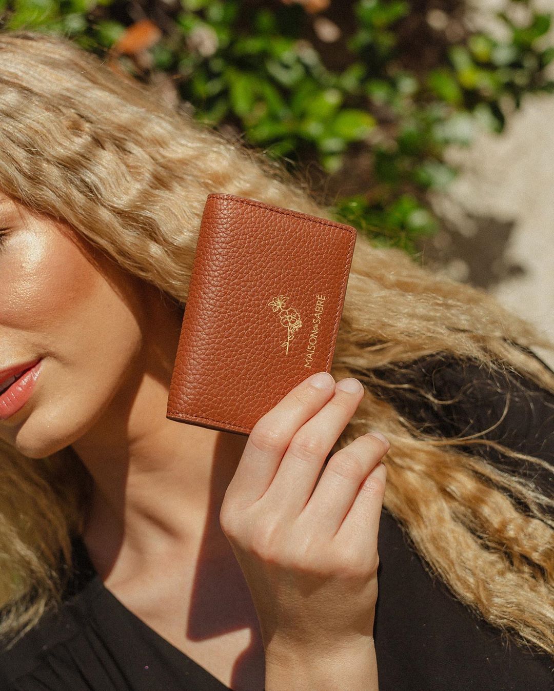 A blonde woman holds a stunning brown wallet up to the sun.