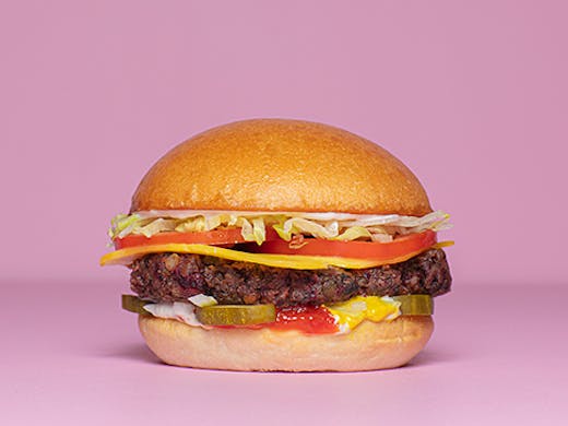 A burger with cheese lettuce tomato and pickles against a pink backdrop