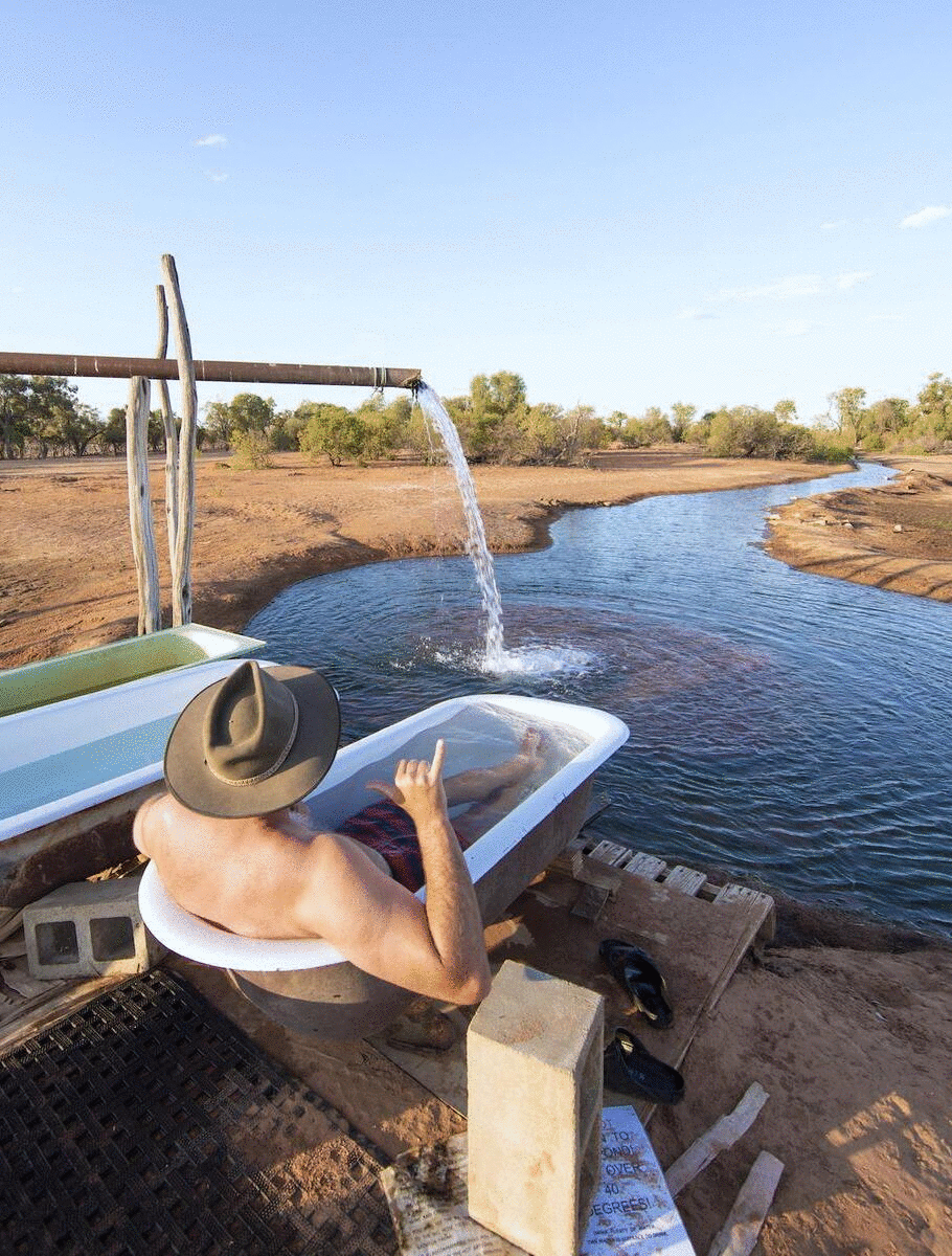 A man sits in an old bathtub near a creek in the golden outback.