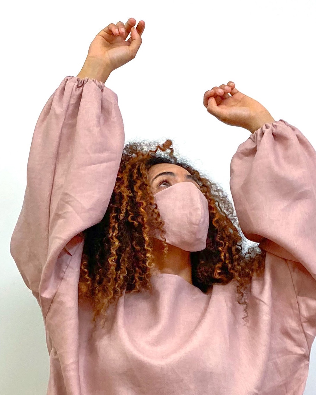 A woman wears a dark pink linen dress with balloon sleeves and a matching face mask. 