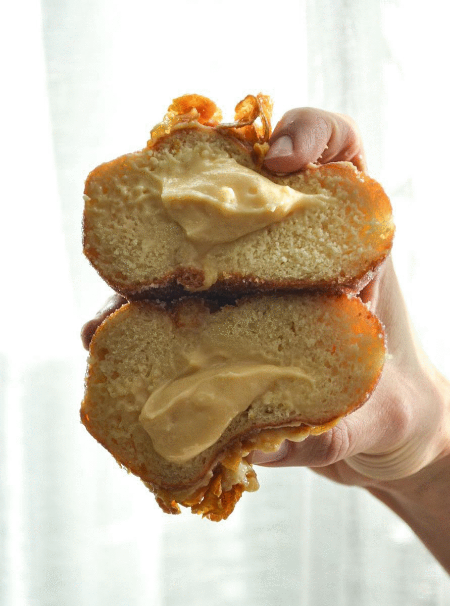 A hand squeezes on two caramel filled donuts. 