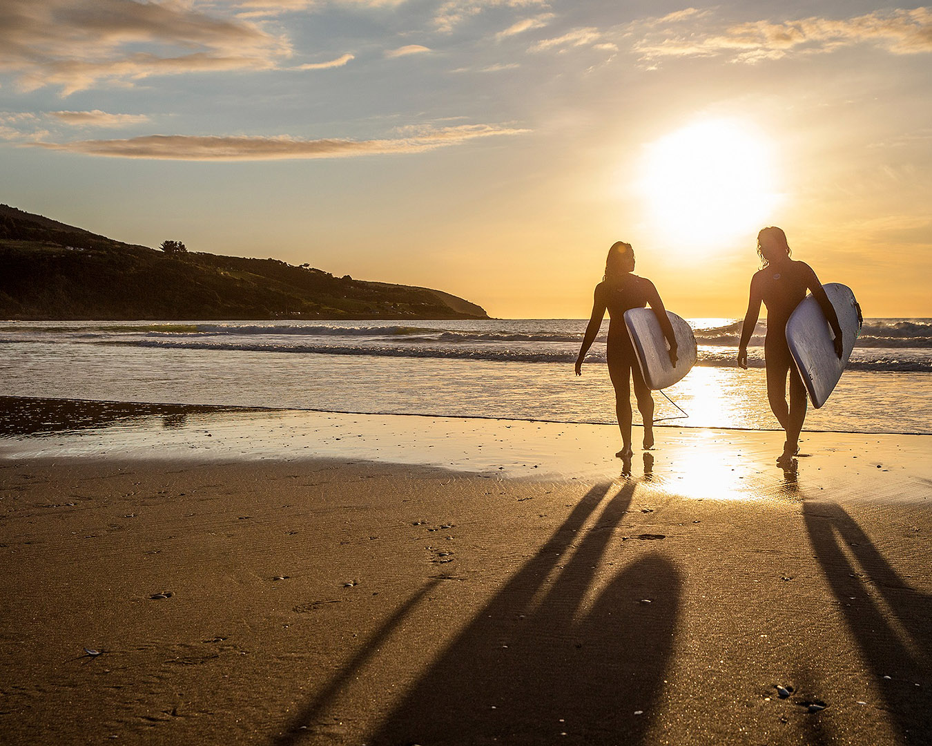 Two people with their surfboards on Ngarunui Beach.