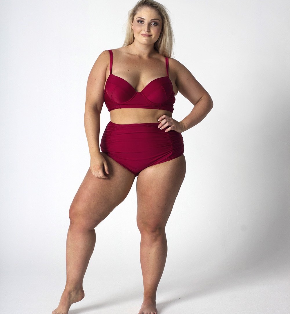 A plus sized blonde woman wears a high-waisted, red wine bikini. 