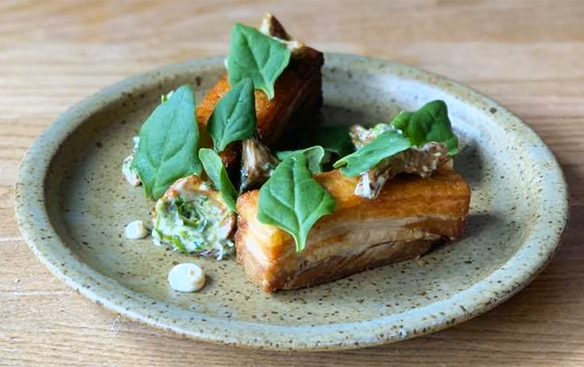 Delicious looking pork belly topped with green leaves sits on a plate at Sherwood.