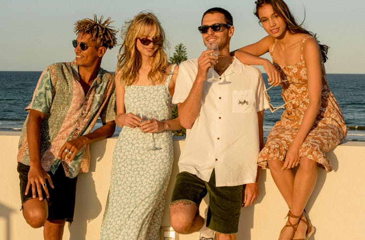 Two women and two men stand by the beach wearing chic coastal wear.