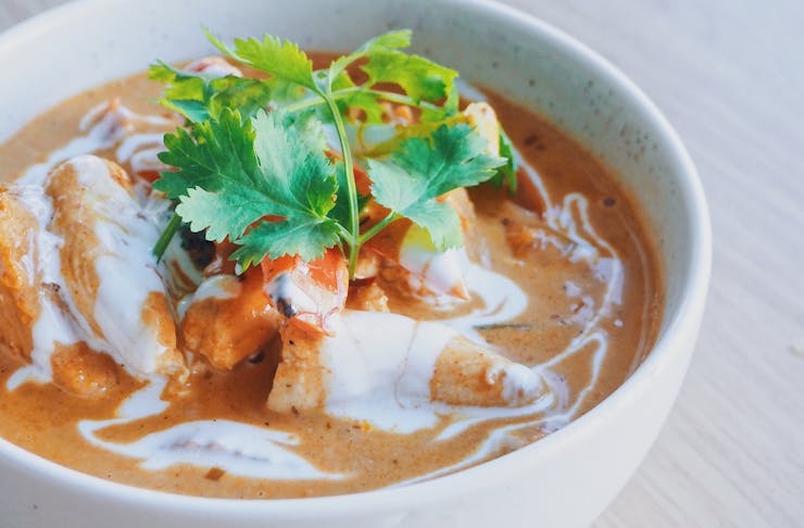 A bowl of mouthwatering orange curry sits on a table waiting  to be devoured.