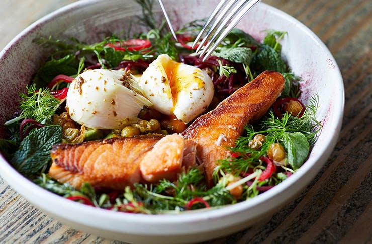A bowl of salad with grilled salmon and two poached eggs on top. 