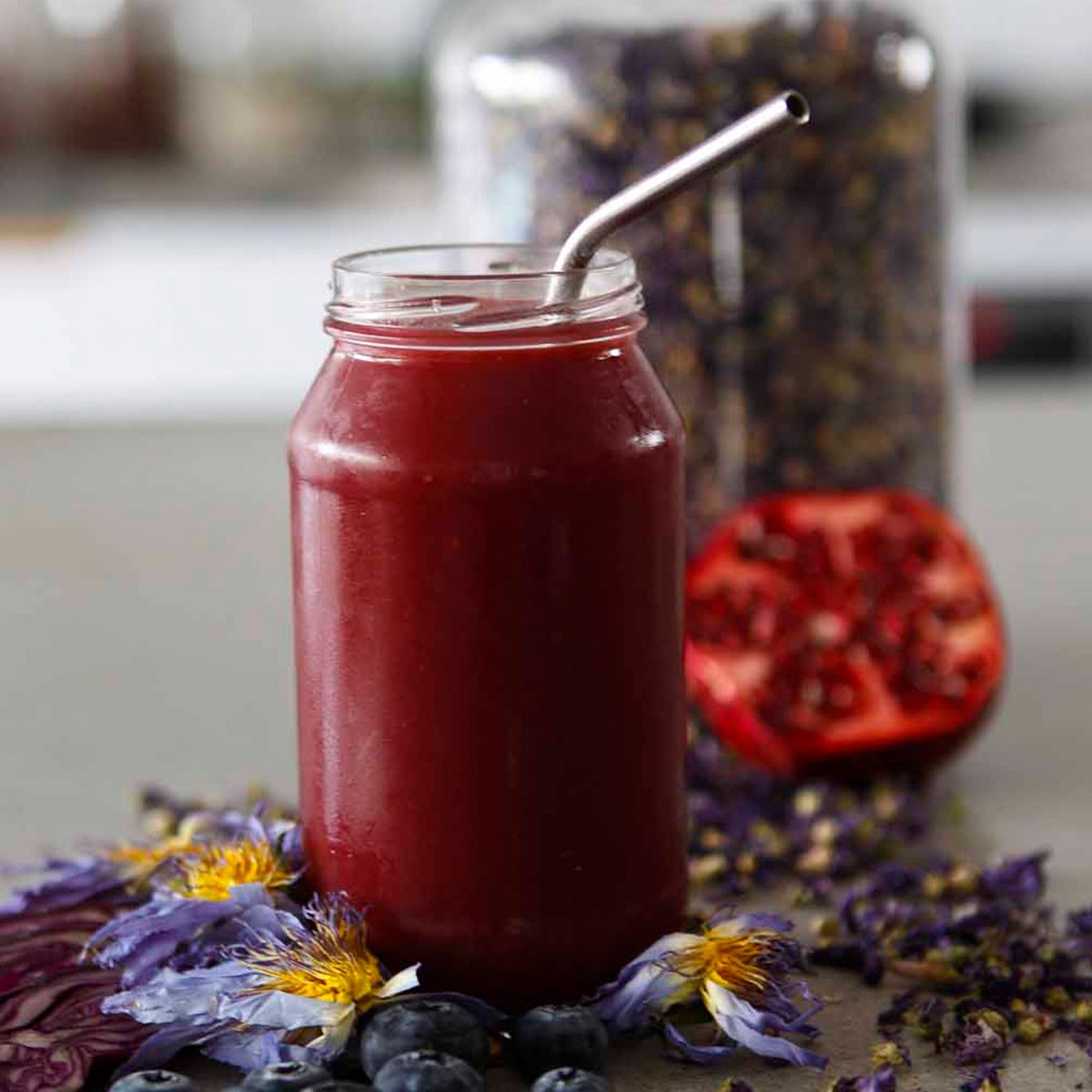 a deep maroon smoothie in a glass jar in front of a jar full of potpourie