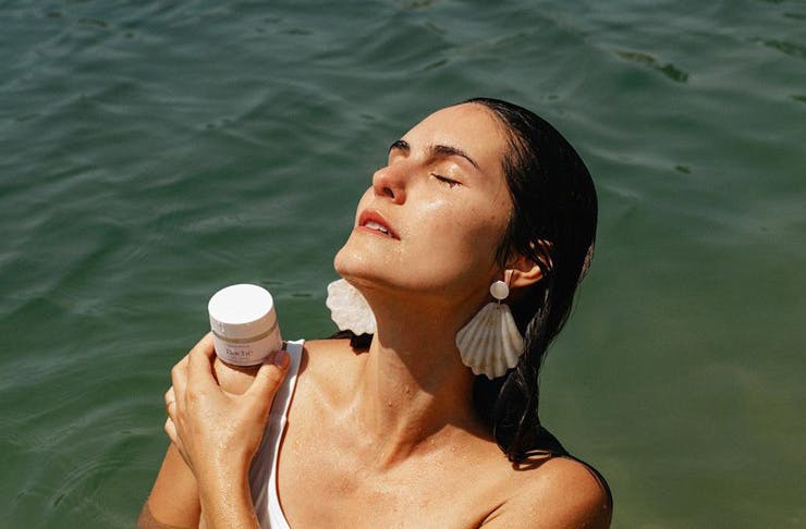 A woman poses in the ocean with a bottle of Bache de Mar serum.