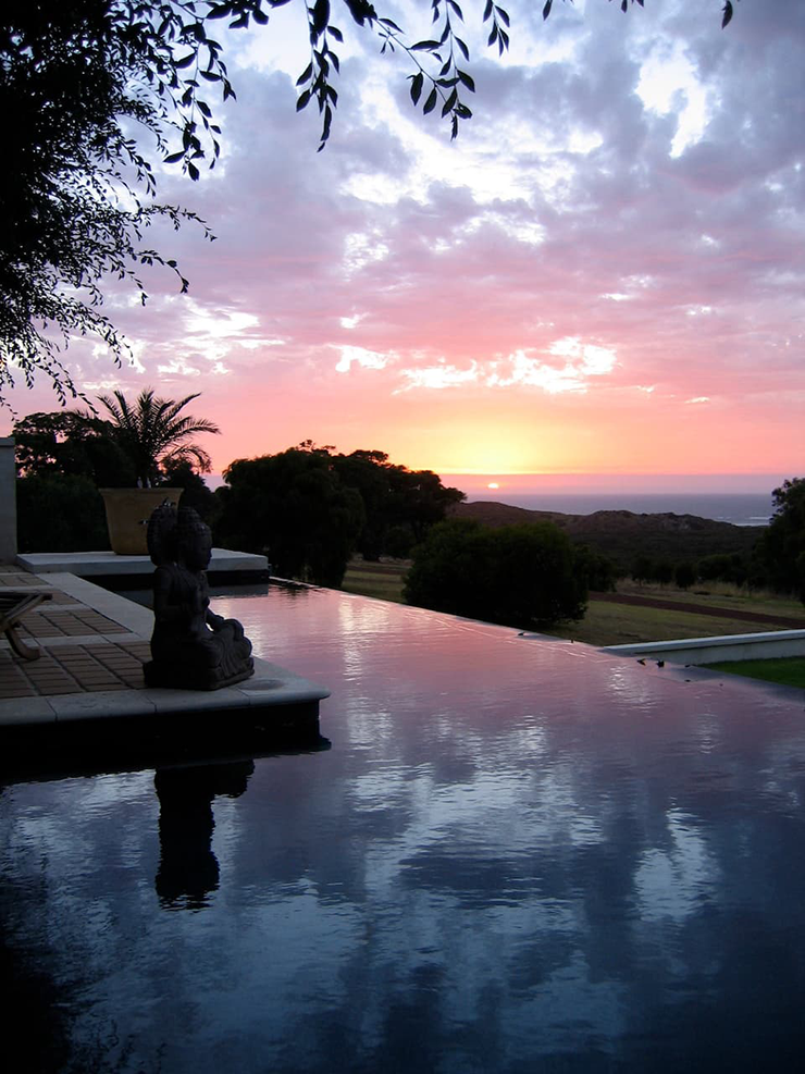An infinity pool drenched in crimson tones from the evening sun.