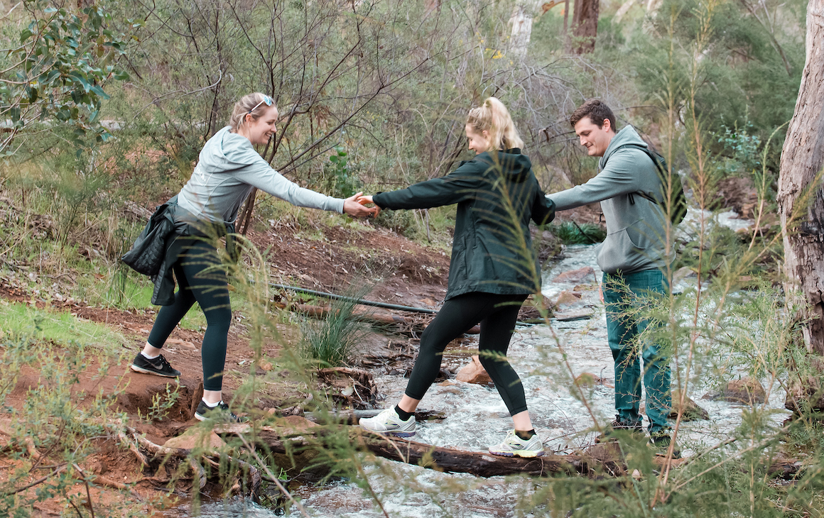 three people help each other cross a small flowing stream