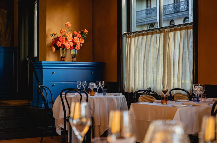 The dining room at Ursula's restaurant in Sydney; you can see tables with white table cloths and a painted blue chest of drawers with a vase of fresh flowers on top. 