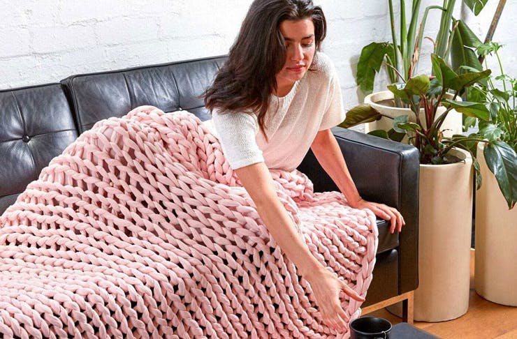 A woman reclining on a couch with a pink woven weighted blanket. 