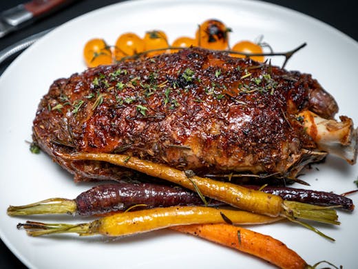 A slow roasted whole lamb shoulder served with Dutch carrots on a white plate. 