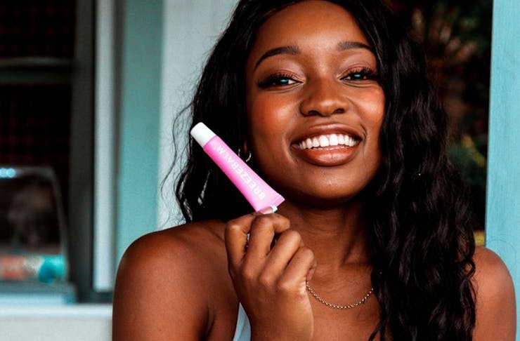 A woman smiling and holding a tube of Breeze Balm lip balm