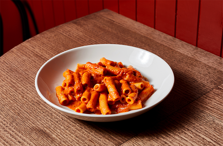 A white bowl of pasta with red sauce on top. The bowl sits on a rustic wooden table.