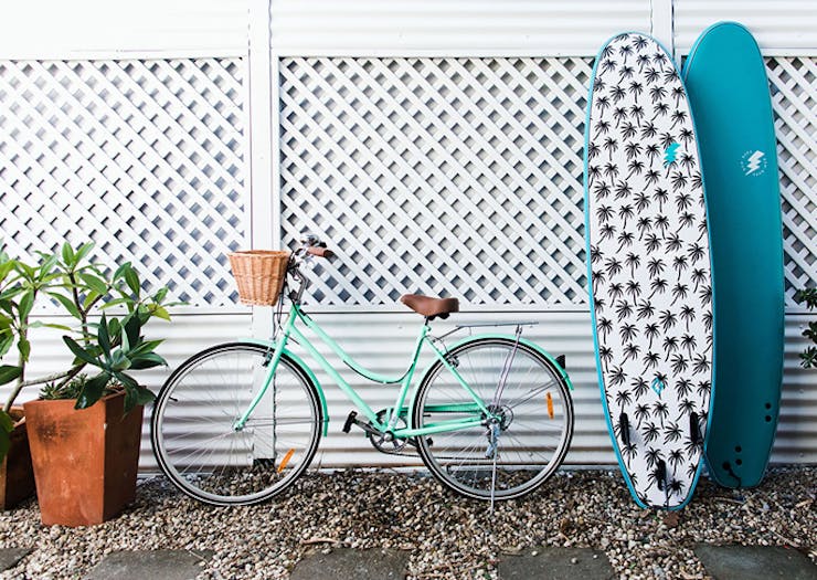 Two surfboards and a turquoise cruise bike lean up against a white wall.