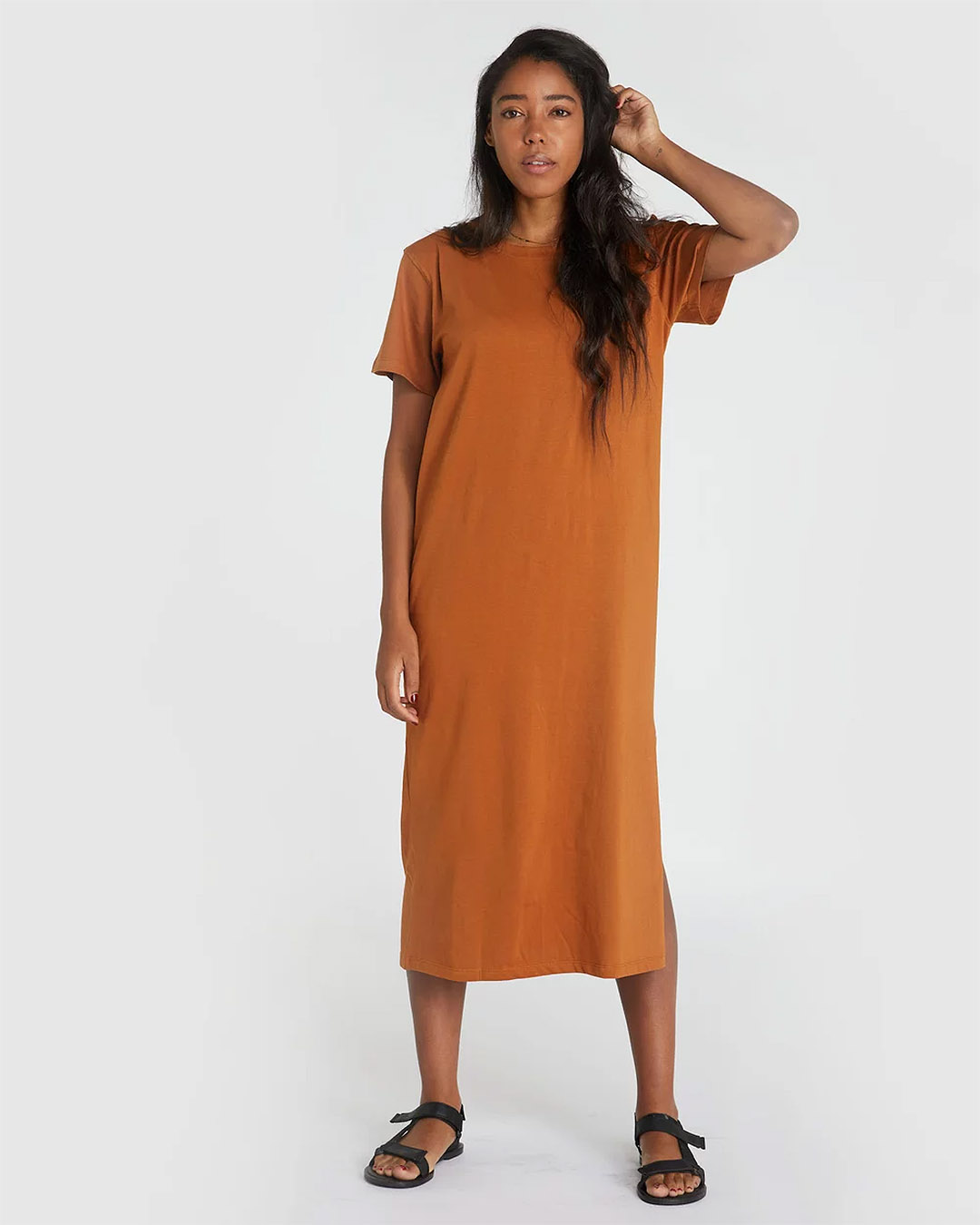 A head-to-toe shot of a woman wearing a burnt orange midi t-shirt with sandals. 