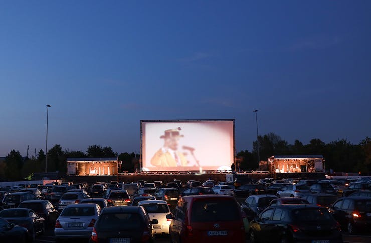 Cars parked in front of cinema screen.