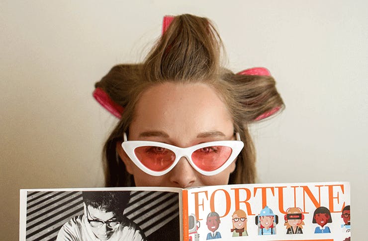 A lady wearing hair rollers and sunglasses reads Fortune magazine.