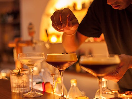 A bartender sprinkles coffee beans on a row of espresso martinis.