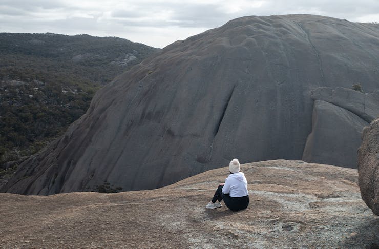 a person sitting on a rock face looking out at mountains