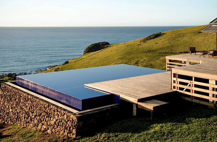 A square infinity pool on a grass hill overlooking the ocean.