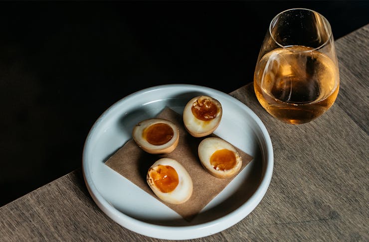 halved pickled eggs on a plate with a glass of wine