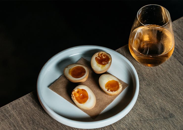 halved pickled eggs on a plate with a glass of wine