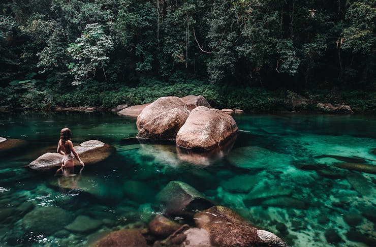 a woman in a crystal clear creek fringed by rainforest