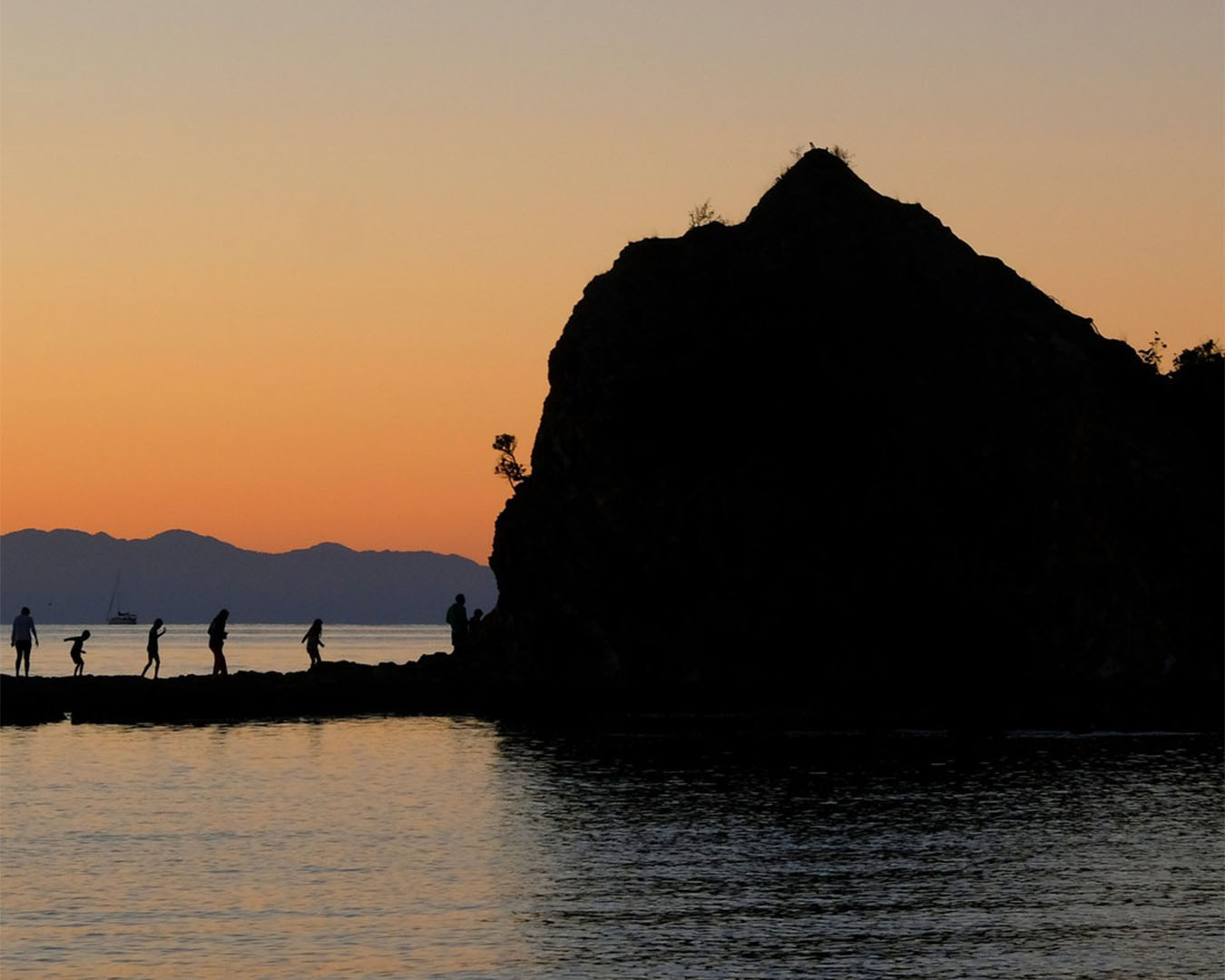 Several people rock hop on an island in Rotoroa at sunset. 