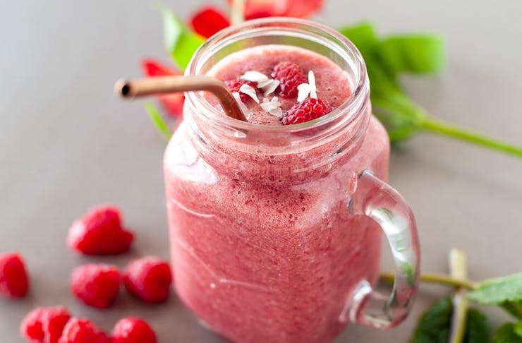 a pink smoothie in a mason jar with raspberries on top