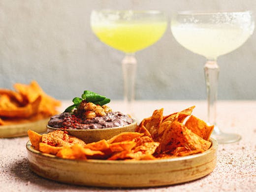 A plate of black bean dip with corn chips and margaritas. 