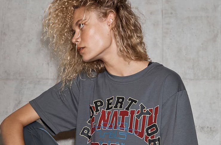 A model with curly hair wearing a grey P.E Nation shirt. 
